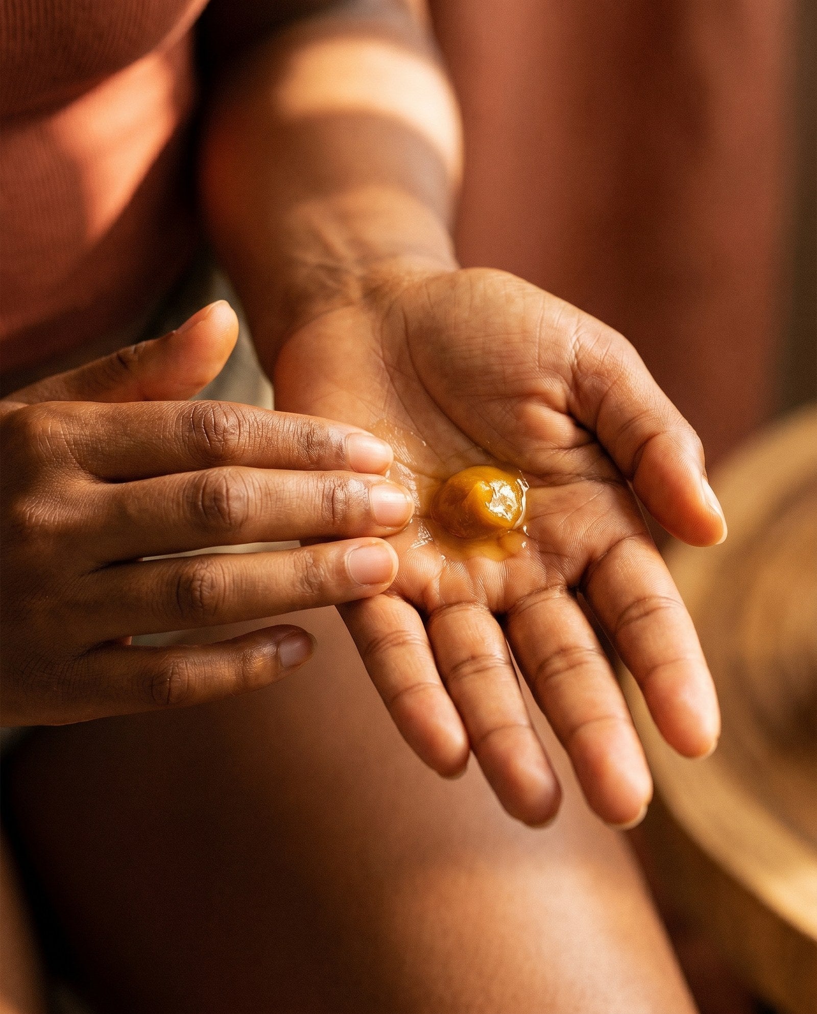 Two hands cupped together holding a small pool of warm amber botanical oil